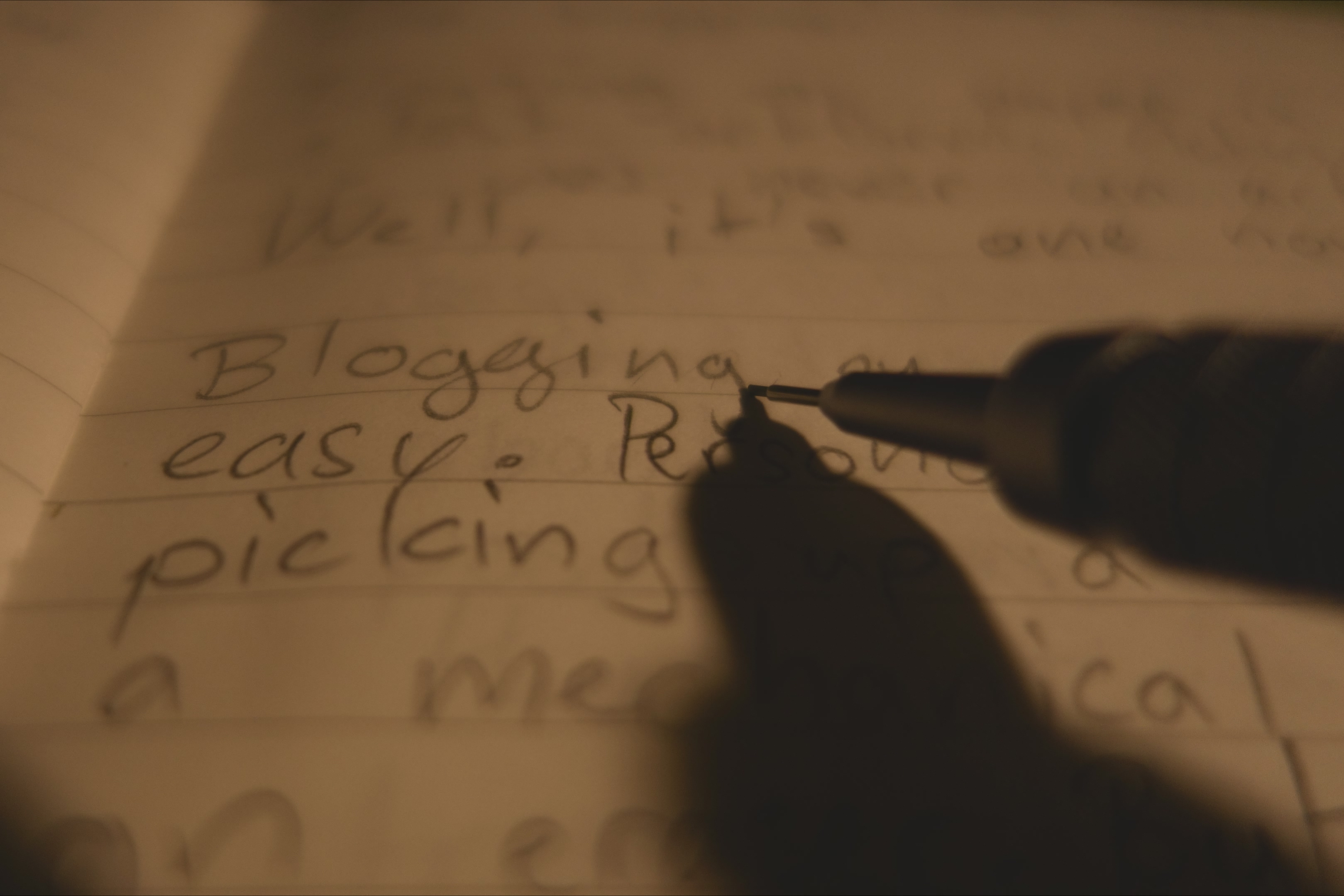 Text in a notebook, 'blogging', with a pencil appearing to be writing.